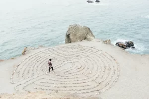 Personne parcourant un labyrinthe de pierres sur le sable près de l'océan, une métaphore du voyage intérieur offert par la kinesiologie holistique.